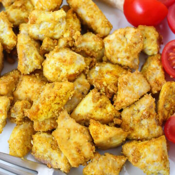 Close up view of eggy tofu pieces on a white plate with tomatoes and fork