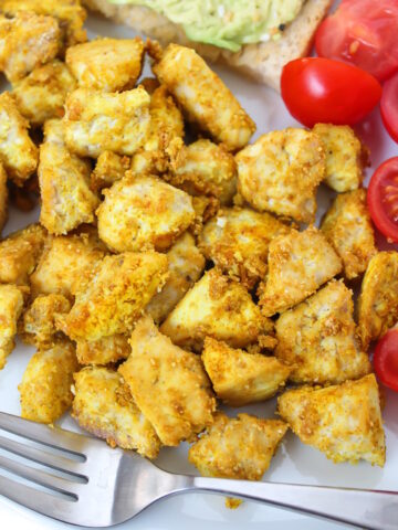 Close up view of eggy tofu pieces on a white plate with tomatoes and fork