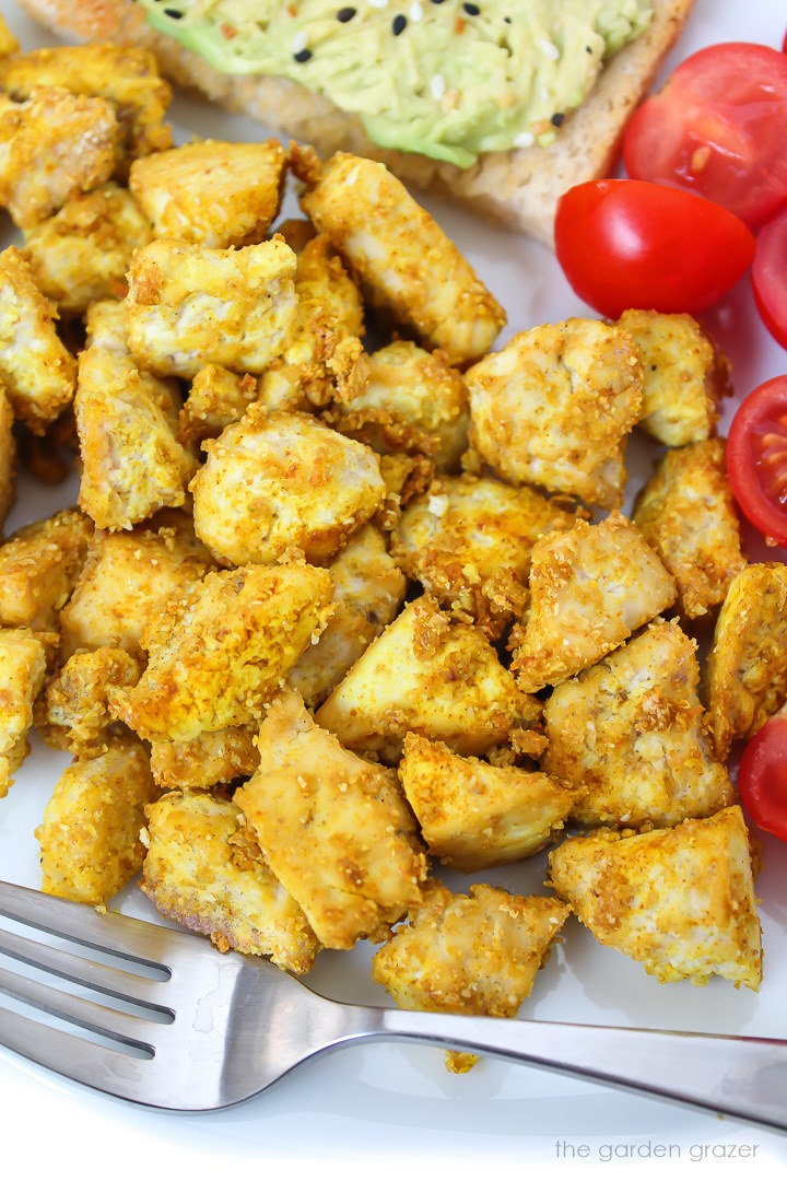 Close up view of eggy tofu pieces on a white plate with tomatoes and fork