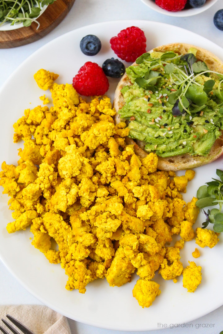 Eggy tofu on a white serving plate with avocado toast and fresh berries