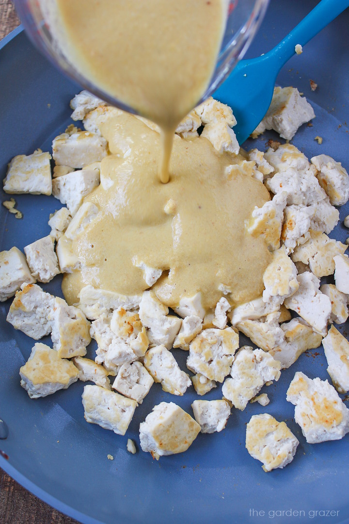 Sauce being poured over tofu crumbles cooking in a skillet
