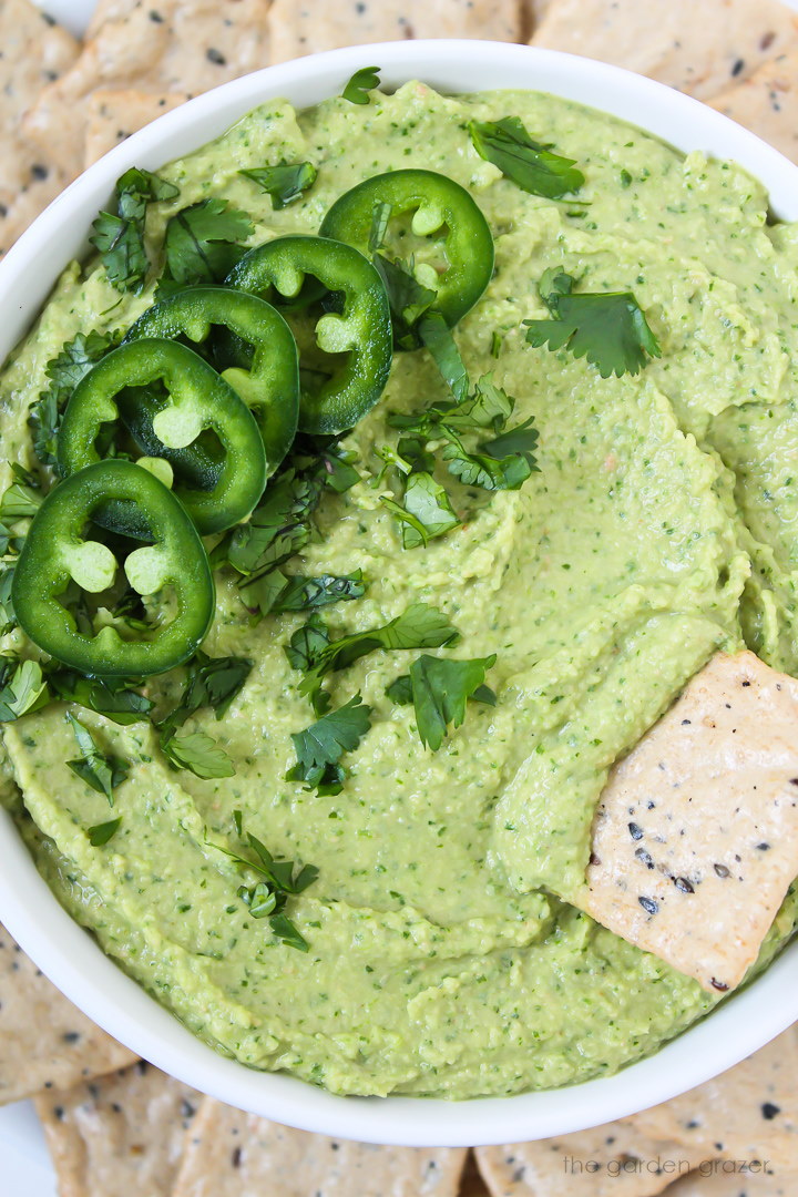 Close up view of cilantro jalapeno hummus in a white bowl with cracker