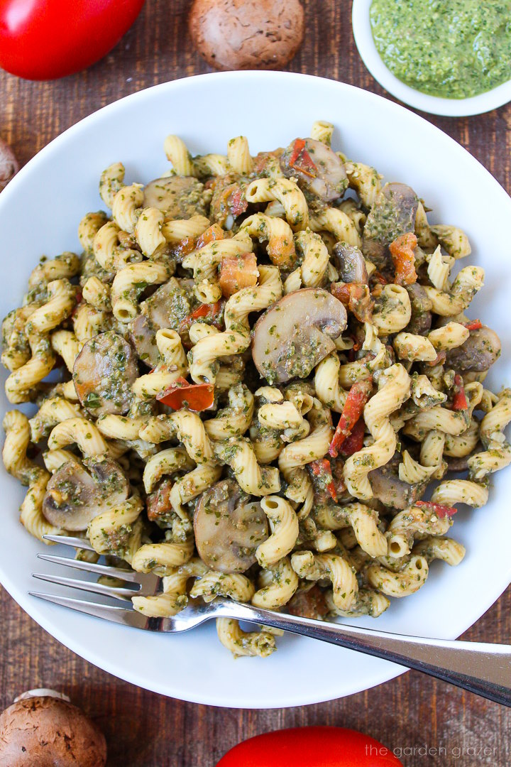 Overhead view of mushroom pesto pasta in a white bowl with serving fork