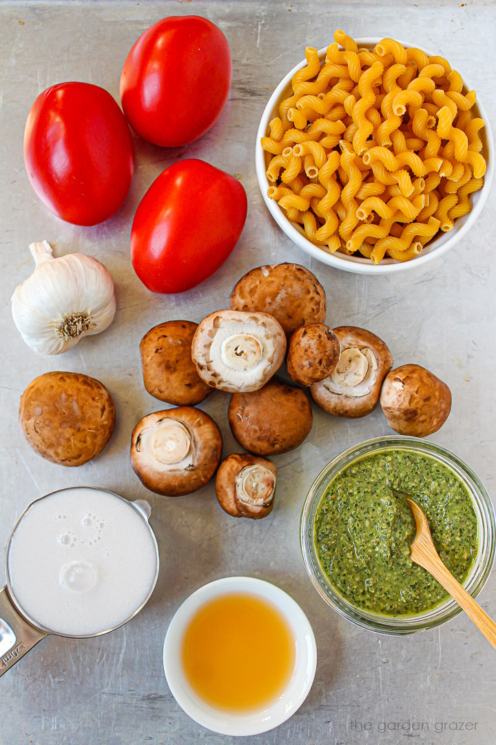 Fresh mushrooms, tomatoes, garlic, vinegar, and dairy-free milk ingredients laid out on a metal tray