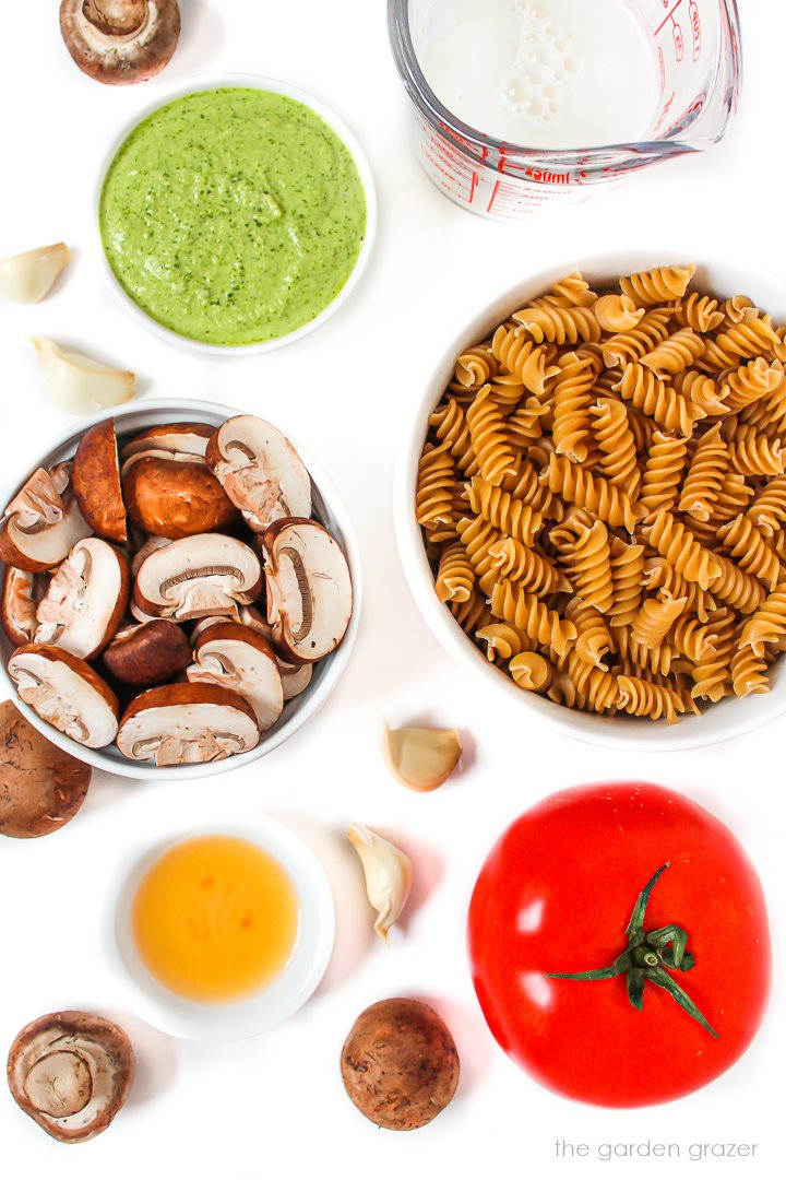 Pasta, tomato, mushrooms, garlic, and milk ingredients laid out on a white table