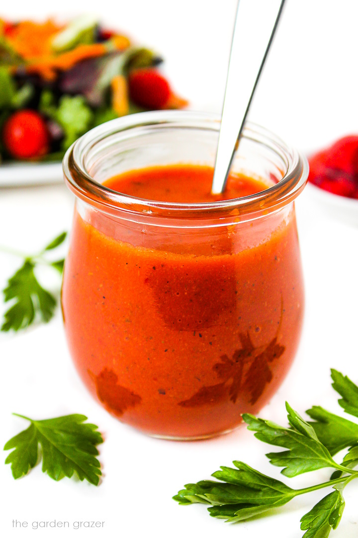 A small glass jar of roasted red pepper salad dressing with serving spoon