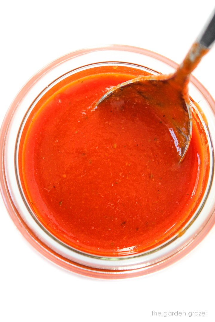 Overhead view of roasted red bell pepper salad dressing in a small glass jar with spoon