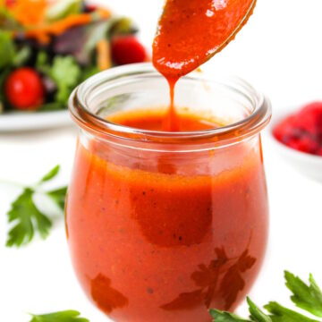 Spoon lifting up roasted red pepper salad dressing from a small glass jar
