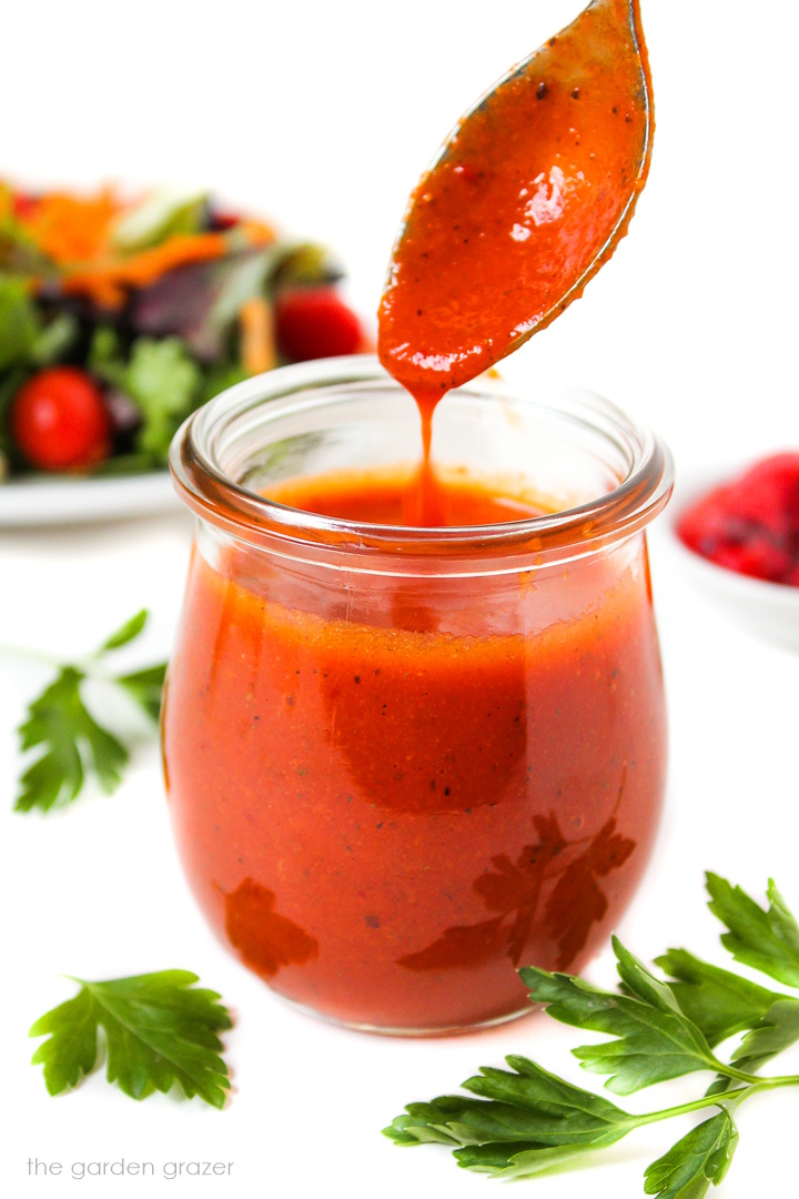 Spoon lifting up roasted red pepper salad dressing from a small glass jar