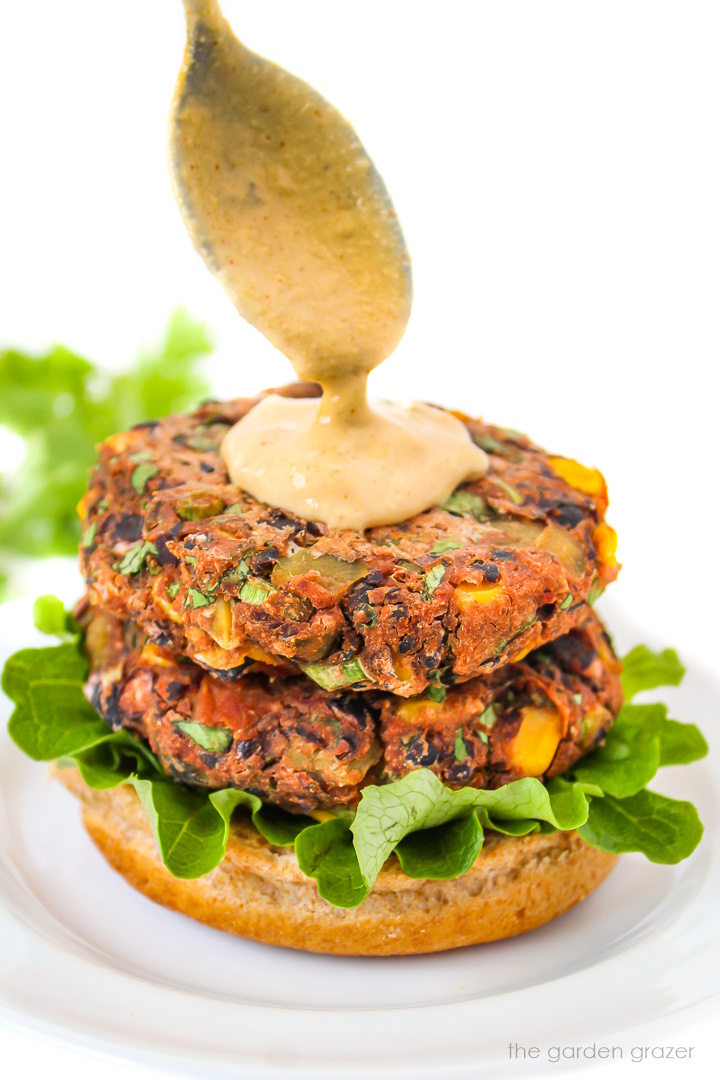 Spooning a creamy sauce over open-faced black bean burger