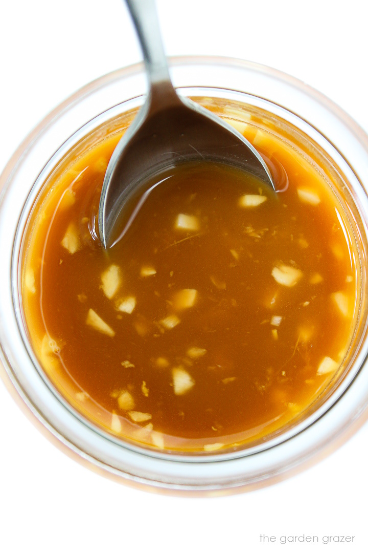 Overhead view of vegan stir fry sauce in a small glass jar with spoon