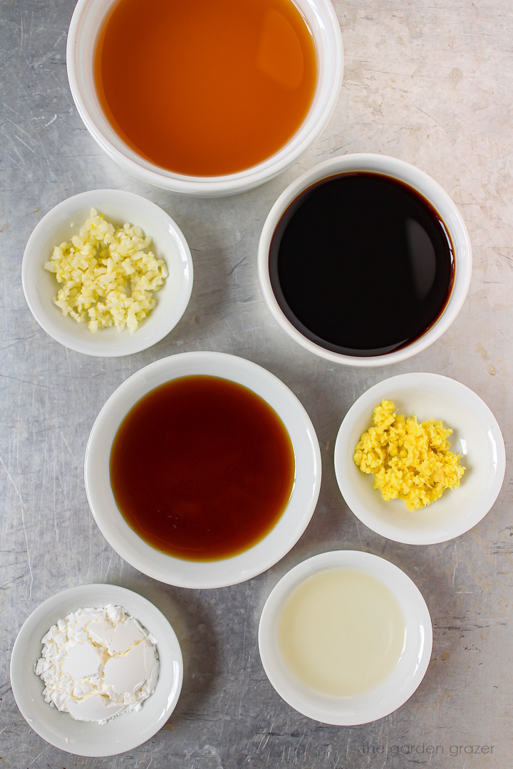 Ginger, garlic, tamari, vinegar, and broth ingredients set out in white bowls on a metal tray