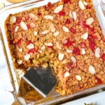 A spatula lifting strawberry baked oatmeal from a baking dish