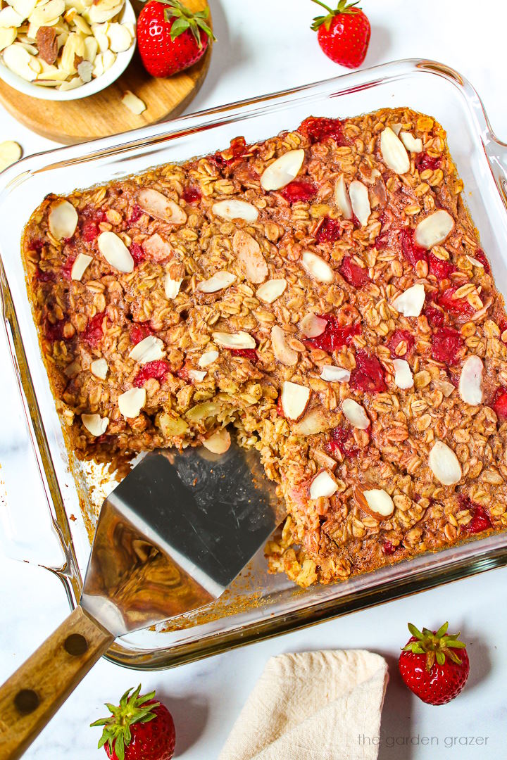 A spatula lifting strawberry baked oatmeal from a baking dish