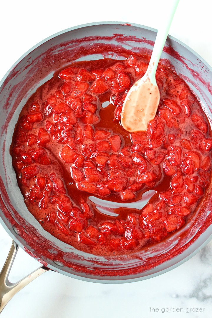 Overhead view of preparing strawberry compote in a pan with a spatula for stirring