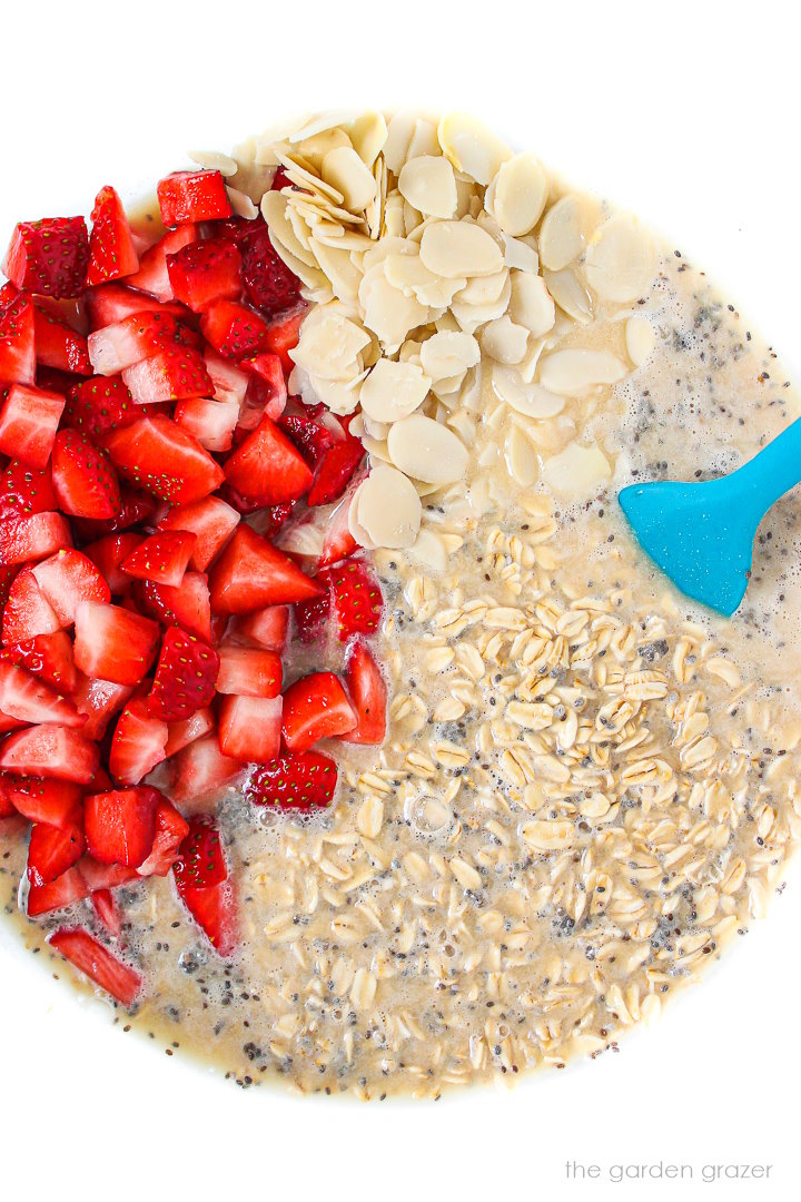 Overhead view of preparing strawberry baked oatmeal in a glass bowl with spatula