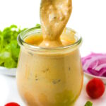 Spoon dipping into a small glass jar of vegan big mac sauce