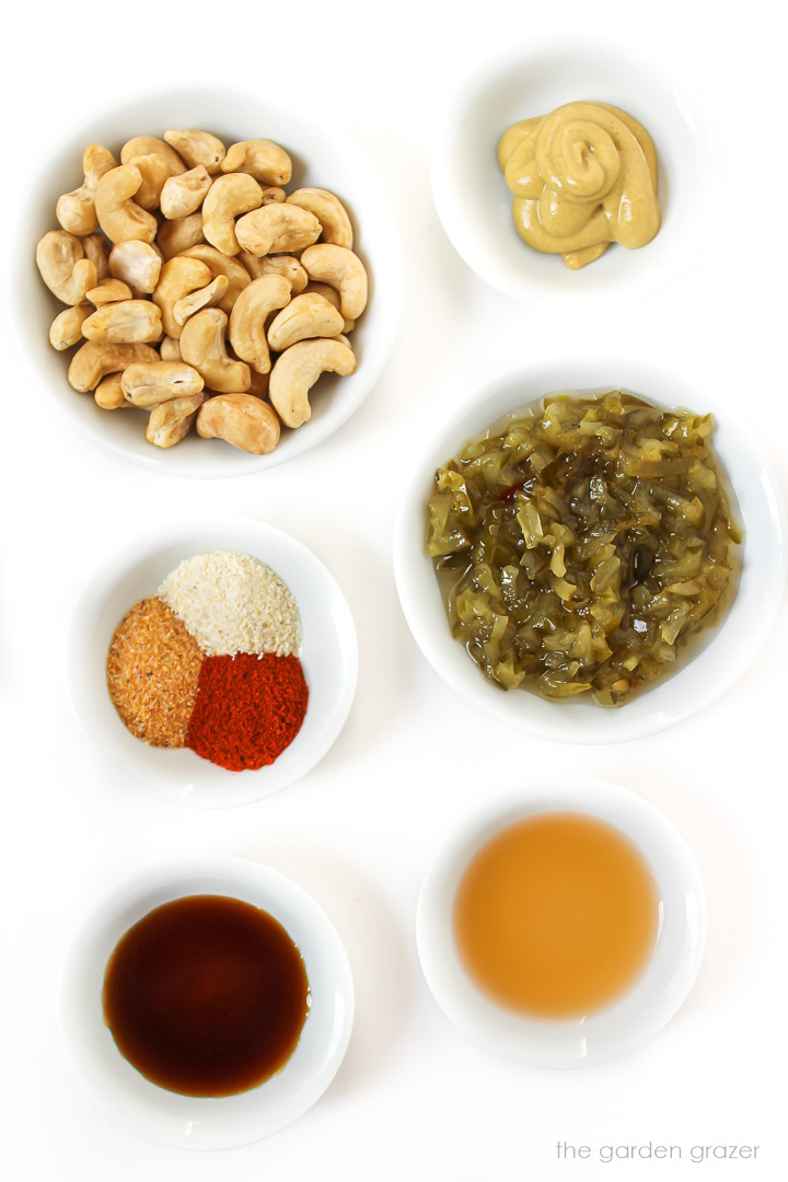 Raw cashews, pickle relish, spices, mustard, and vinegar ingredients laid out in small white bowls