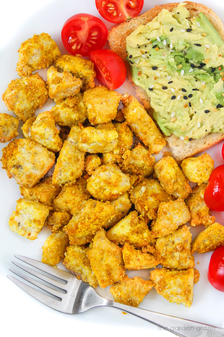 Eggy tofu on a white plate with fork, avocado toast, and tomatoes