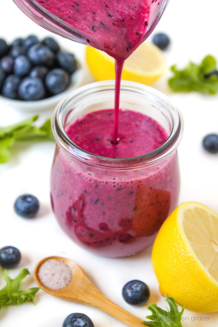 Pouring blueberry salad dressing into a small glass jar