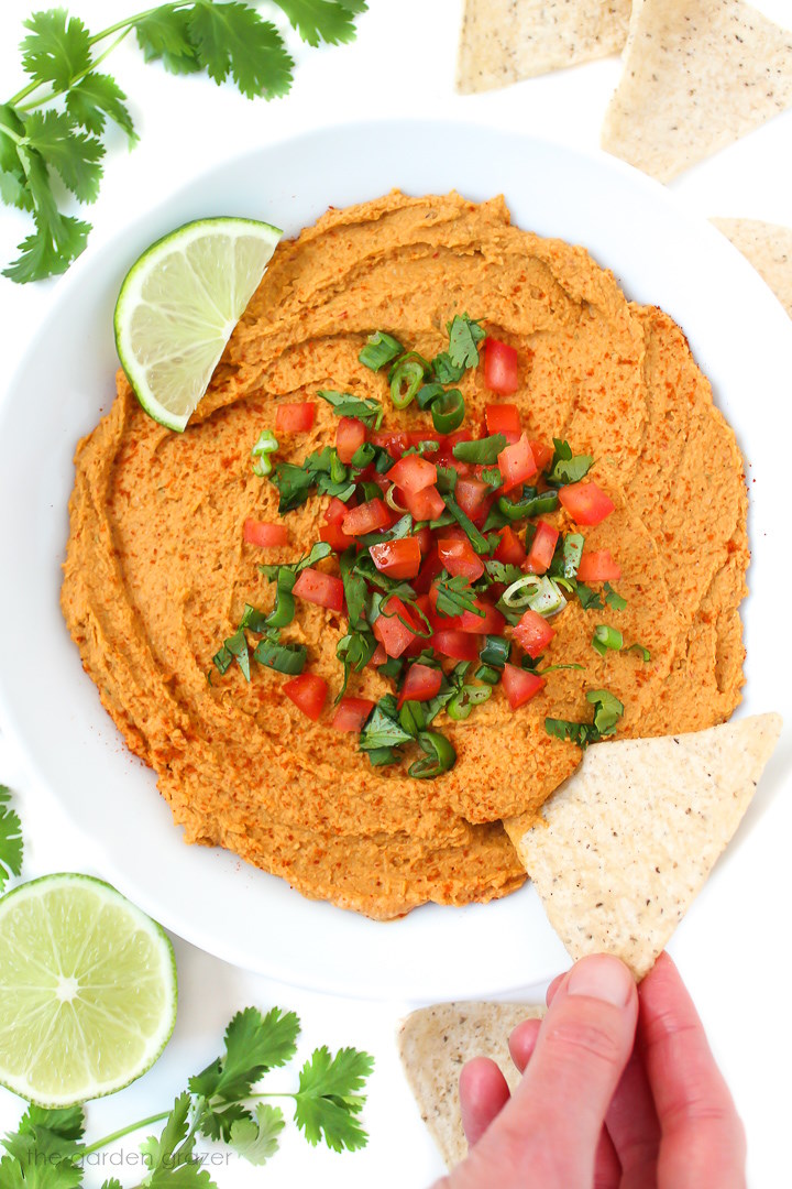 Tortilla chip dipping into a bowl of chipotle taco hummus