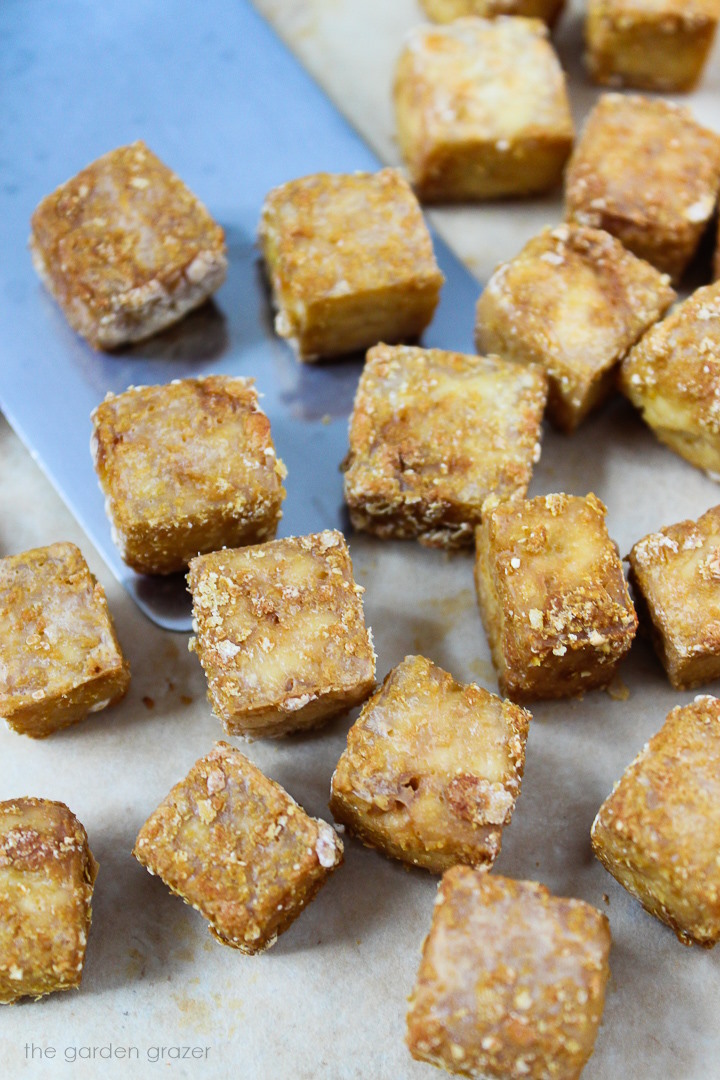 Oil-free crispy tofu baking on a sheet pan with metal spatula