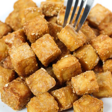 Crispy baked oil-free tofu cubes on a plate with fork piercing one cube