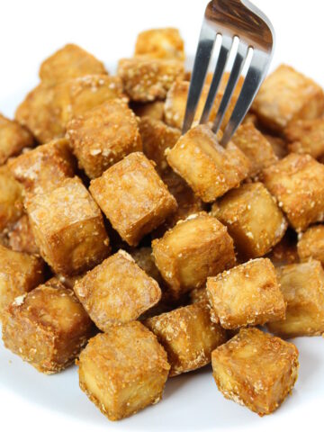 Crispy baked oil-free tofu cubes on a plate with fork piercing one cube