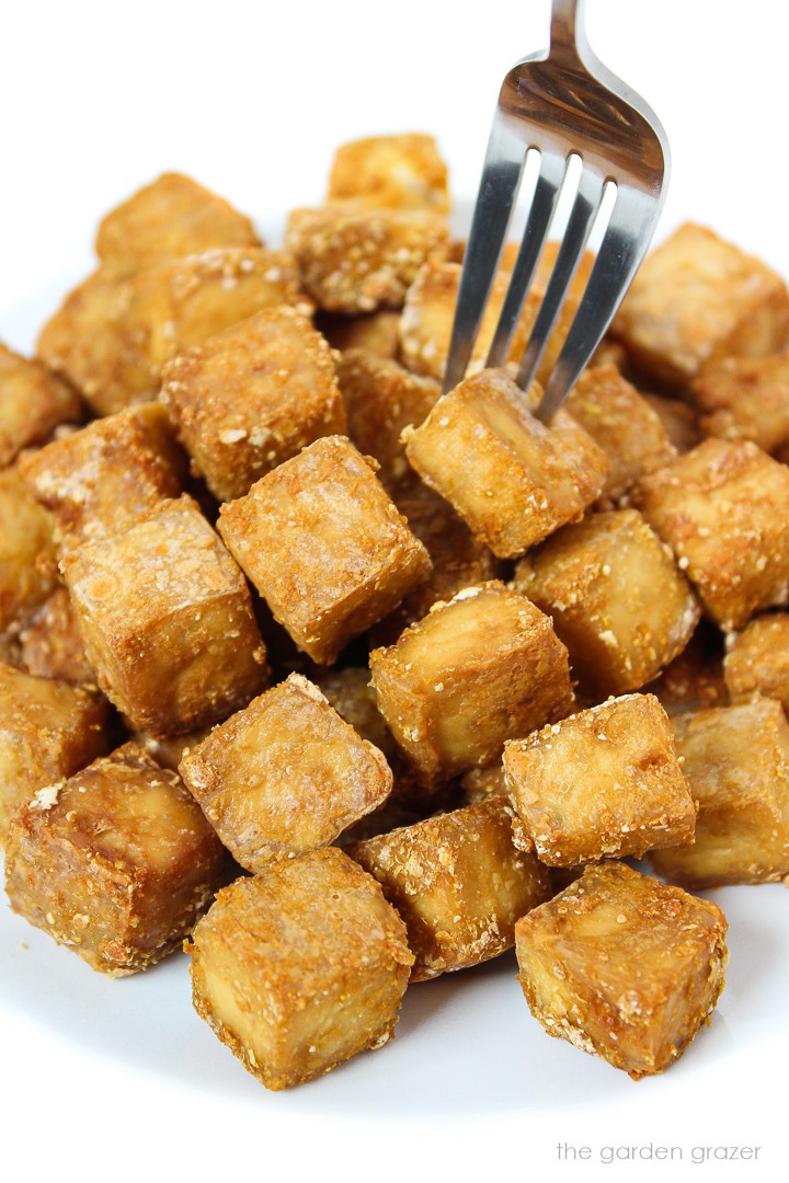 Crispy baked oil-free tofu cubes on a plate with fork piercing one cube