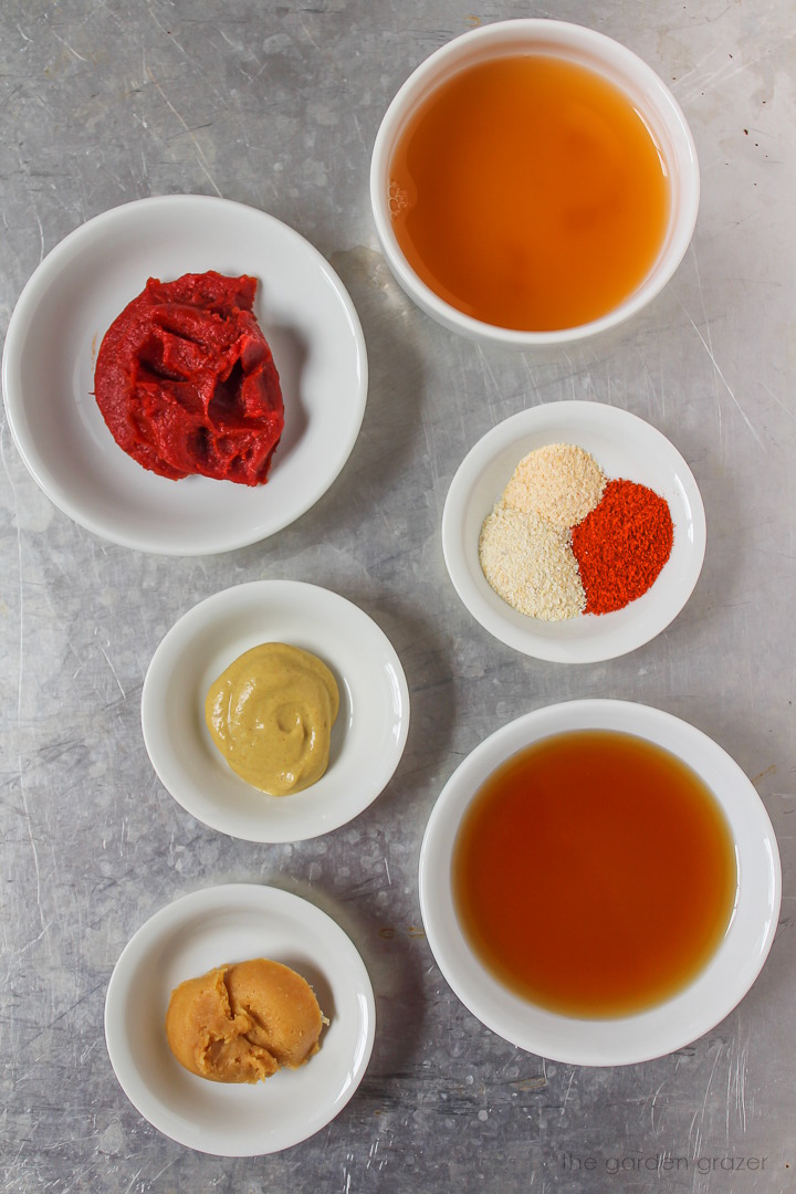 Tomato paste, vinegar, spices, mustard, and miso ingredients in small white bowls on a tray