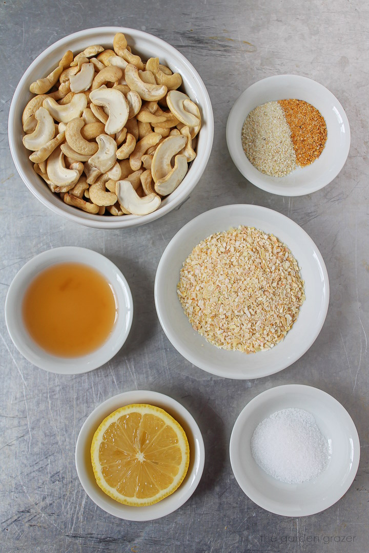 Raw cashews, onion flakes, spices, vinegar, and lemon ingredients set out in white bowls