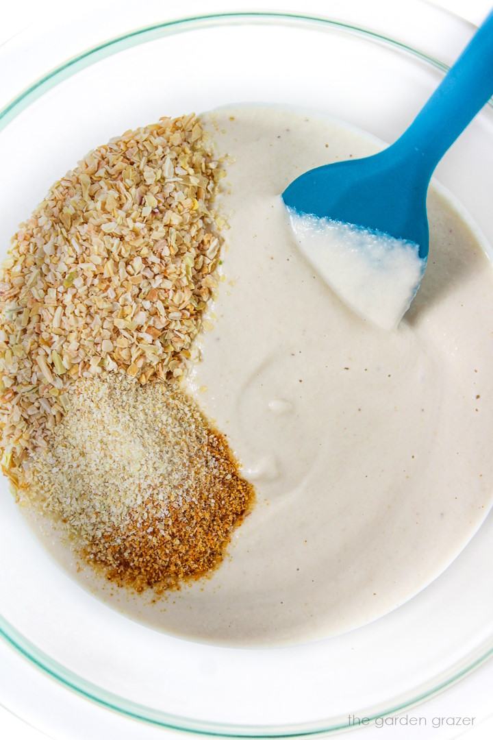 Vegan French onion dip being prepared in a small bowl with blue spatula