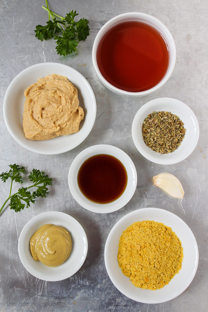 Vinegar, mustard, herbs, hummus, garlic, and nutritional yeast ingredients laid out on a tray