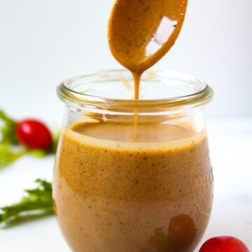 A wooden spoon lifting up maple balsamic dressing from a small glass serving jar