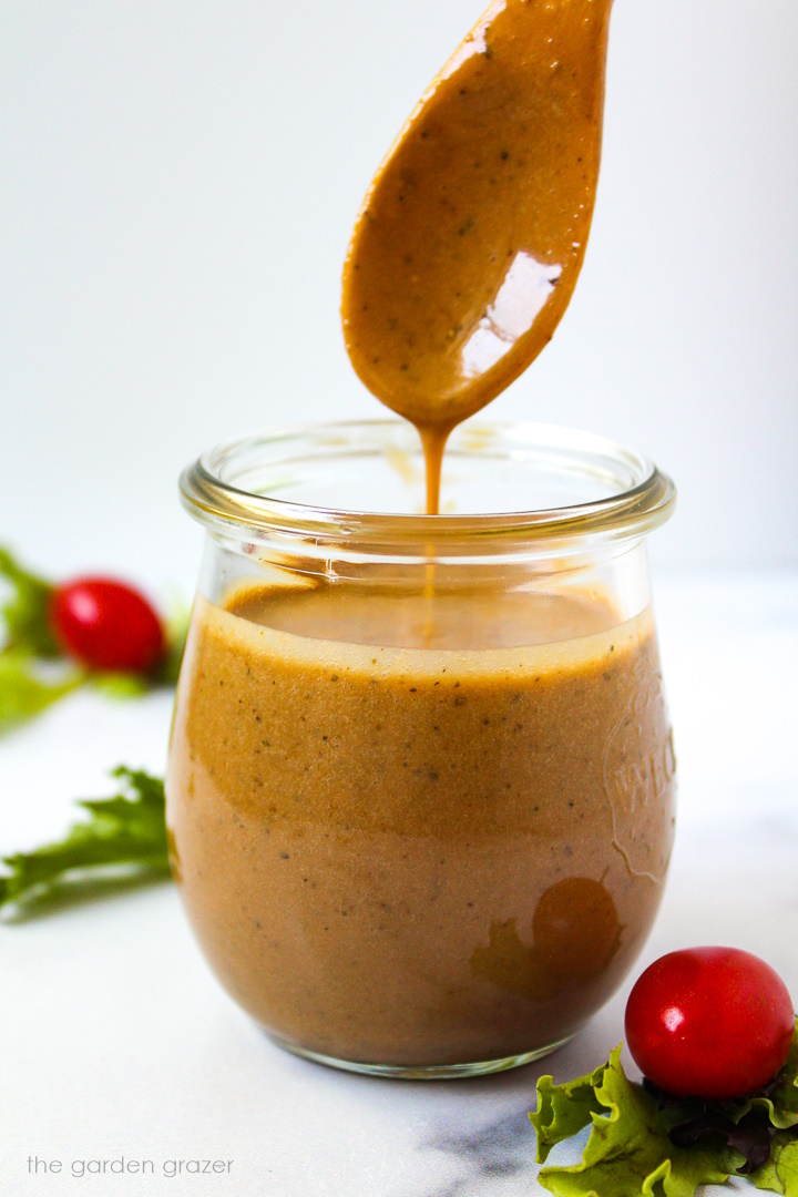 A wooden spoon lifting up maple balsamic dressing from a small glass serving jar