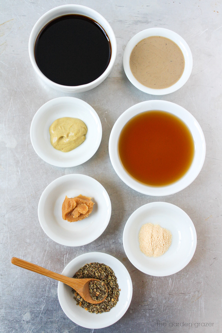Vinegar, syrup, tahini, Dijon mustard, white miso, garlic powder, and seasoning ingredients laid out on a metal tray