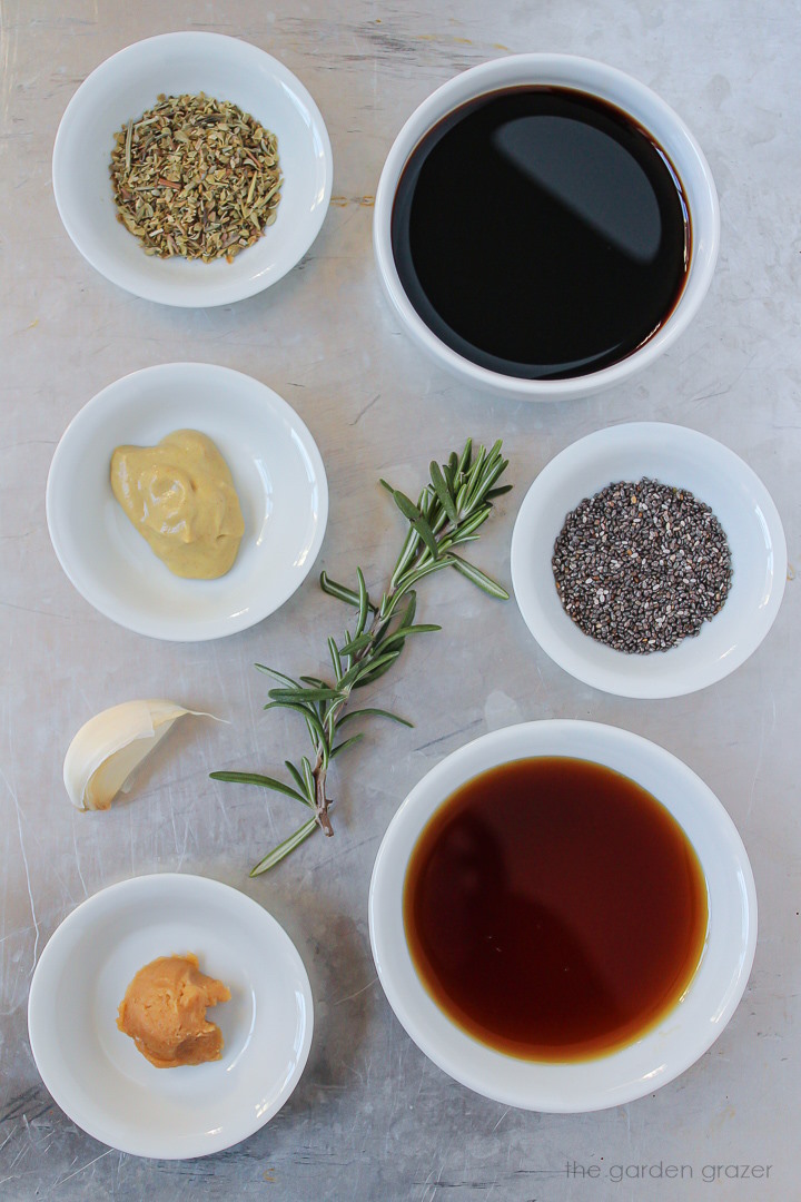 Vinegar, syrup, chia seeds, mustard, garlic, and seasoning ingredients laid out in white bowls