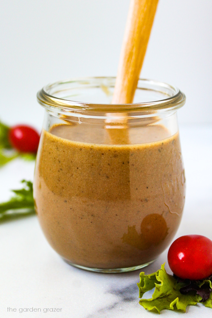 Maple balsamic dressing in a small glass jar with wooden spoon