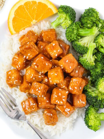 Orange tofu with white rice and steamed broccoli on a white plate