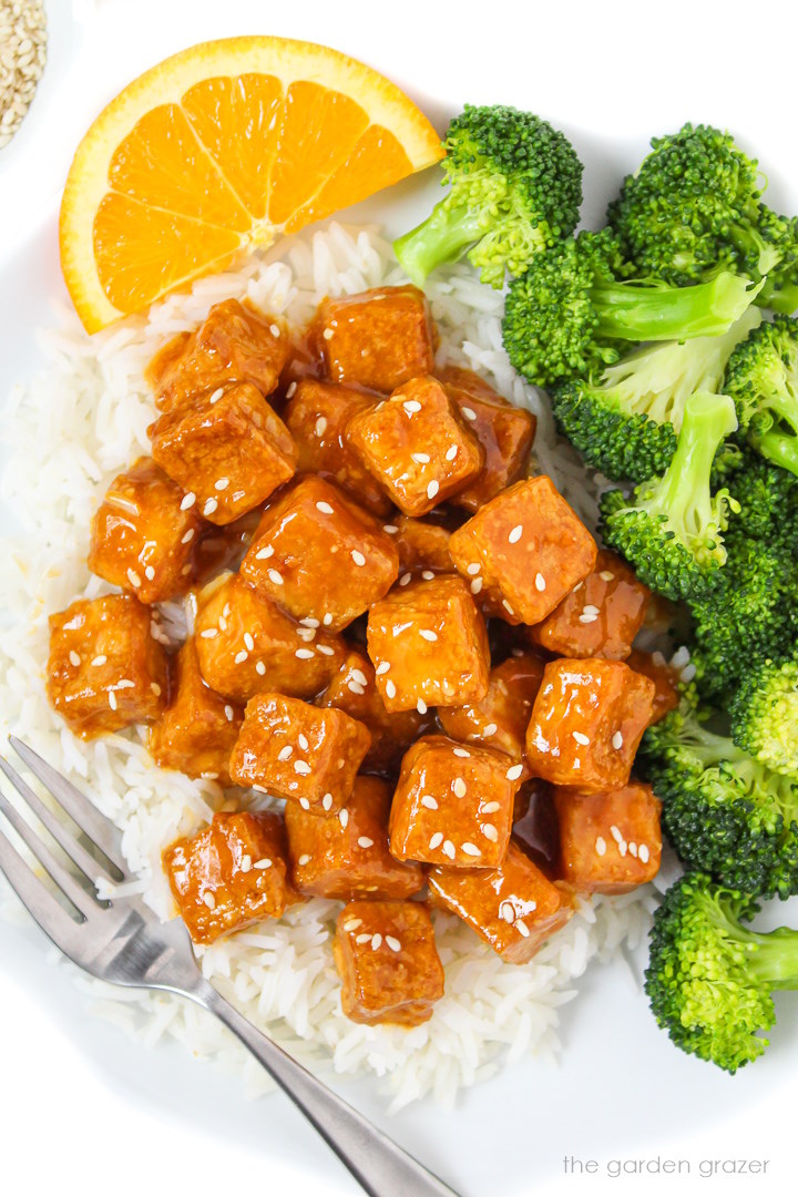 Orange tofu with white rice and steamed broccoli on a white plate