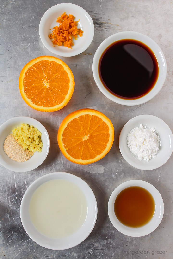 Oranges, tamari, vinegar, garlic, and ginger ingredients laid out in white bowls