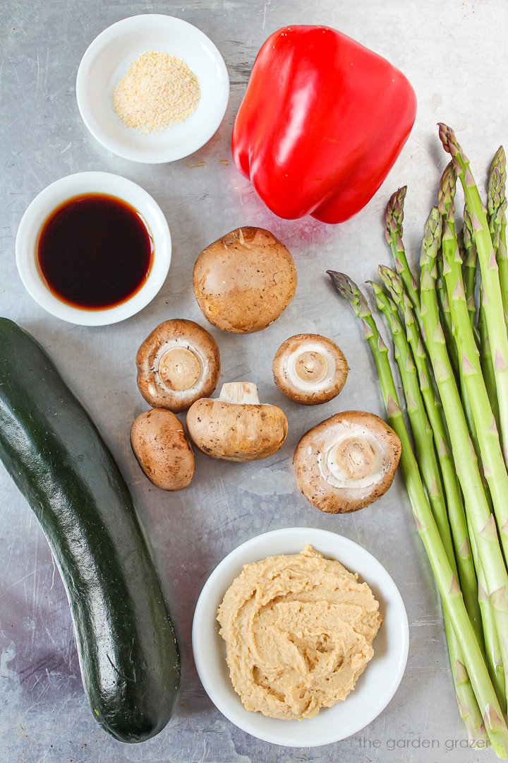 Fresh mushrooms, hummus, vinegar, bell pepper, and asparagus ingredients on a metal tray