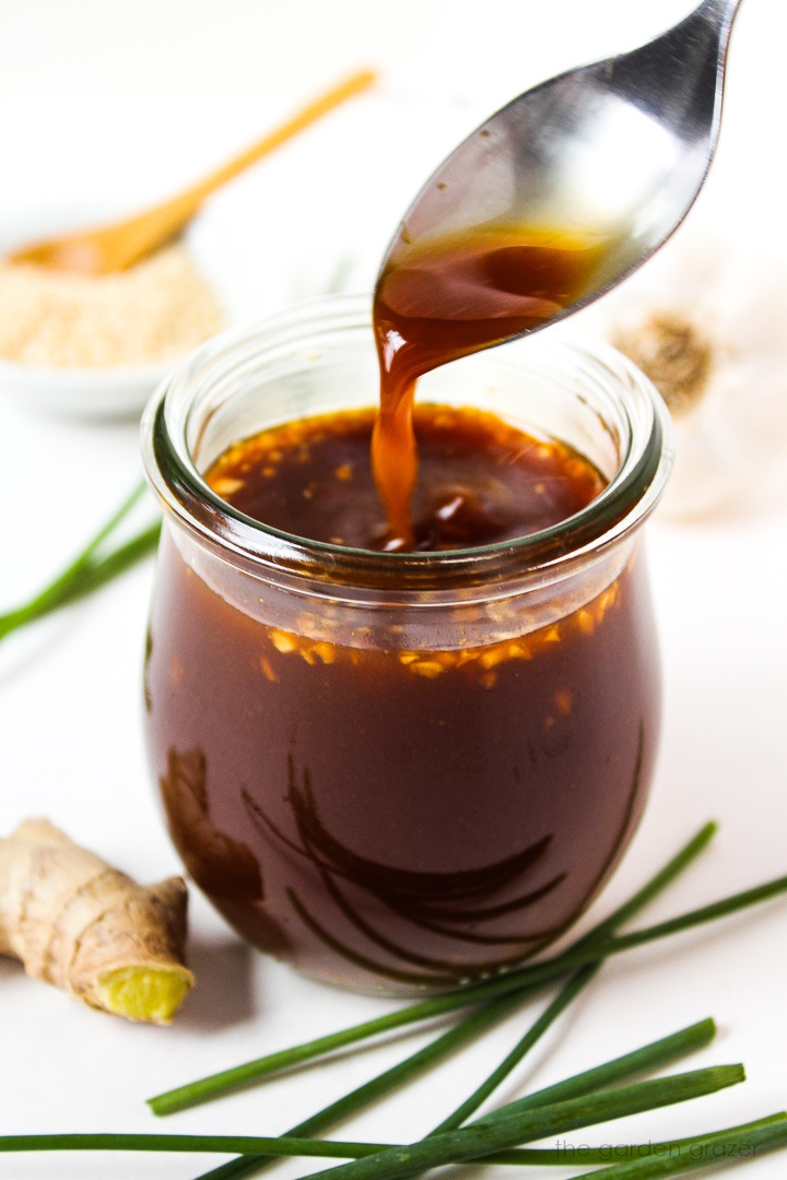 Spoon lifting up vegan stir fry sauce with garlic and ginger from a small glass jar