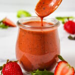 A wooden spoon lifting up strawberry balsamic dressing from a small glass serving jar
