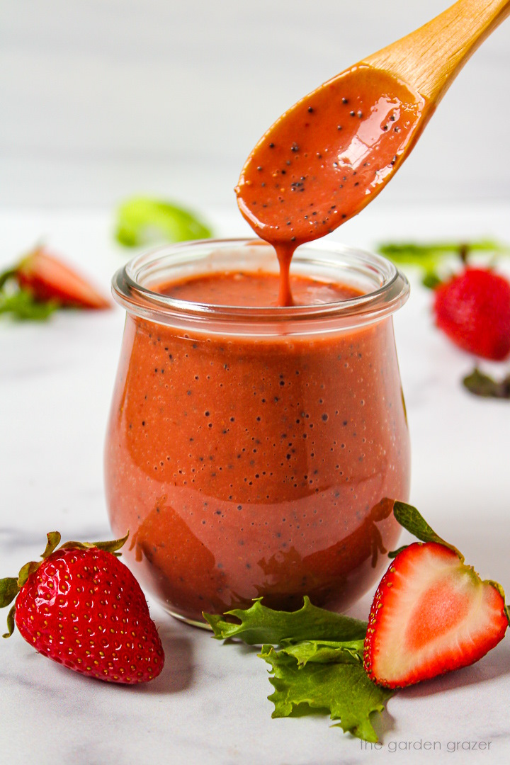 A wooden spoon lifting up strawberry balsamic dressing from a small glass serving jar