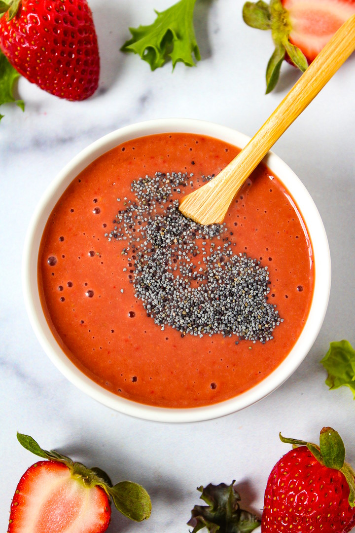 Stirring poppy seeds into blended strawberry balsamic dressing in a white bowl