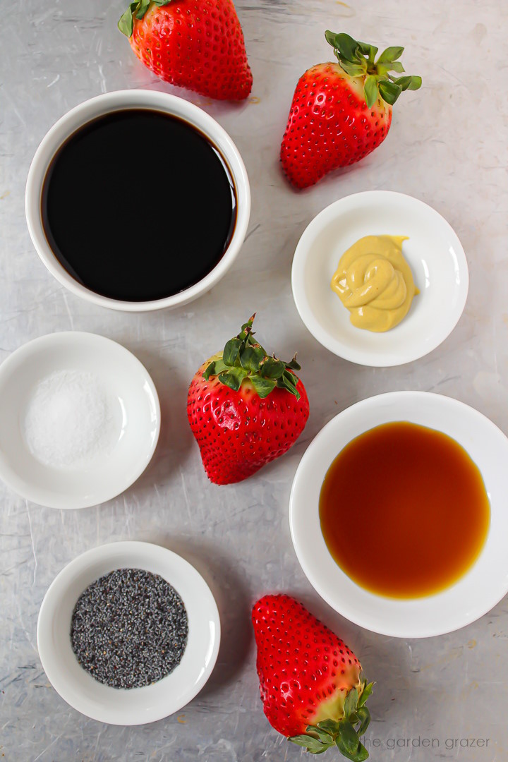 Strawberries, vinegar, poppy seeds, mustard, and syrup ingredients laid out in white bowls