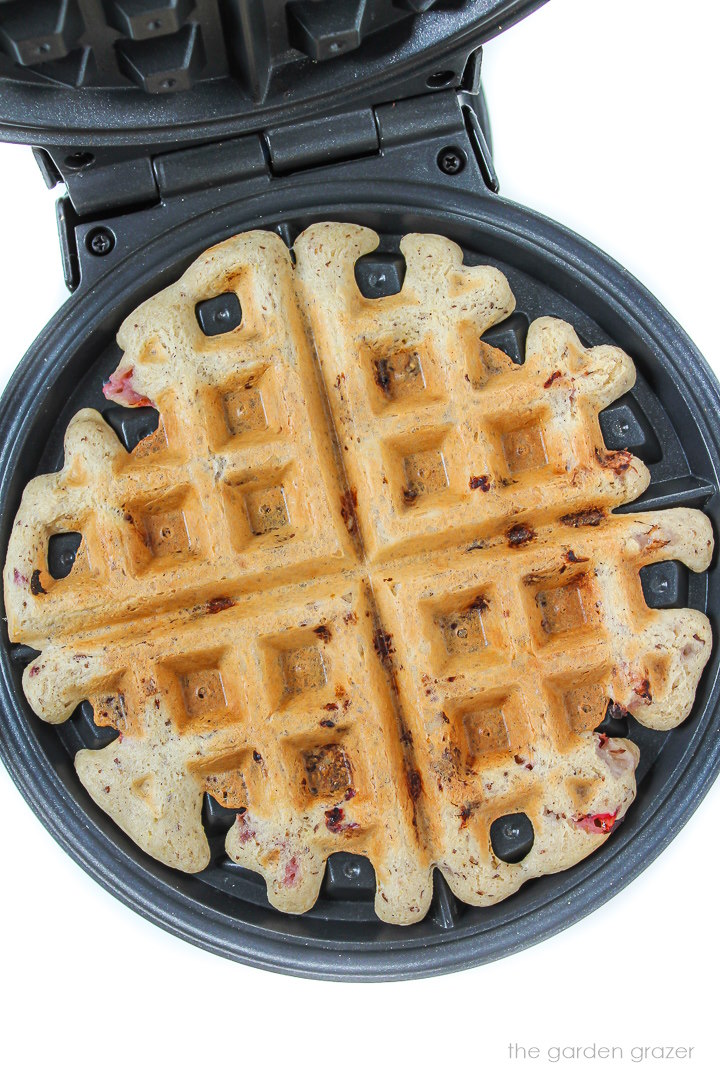 Overhead view of strawberry waffle cooking on a waffle iron