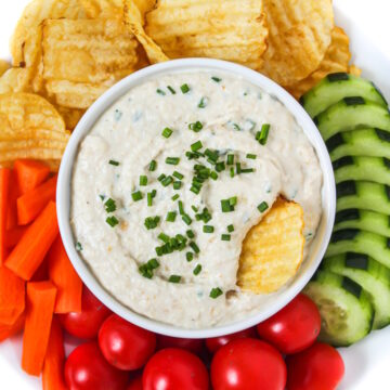 Vegan French onion dip in a white bowl with veggies and chips