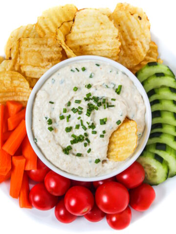 Vegan French onion dip in a white bowl with veggies and chips